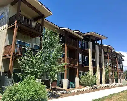 Apartment building exterior with columns, wood panel siding and lush landscaping.